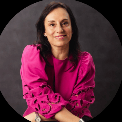 Woman with long dark hair in a bright pink blouse, smiling and seated with arms crossed—perfect for corporate video production Sydney.