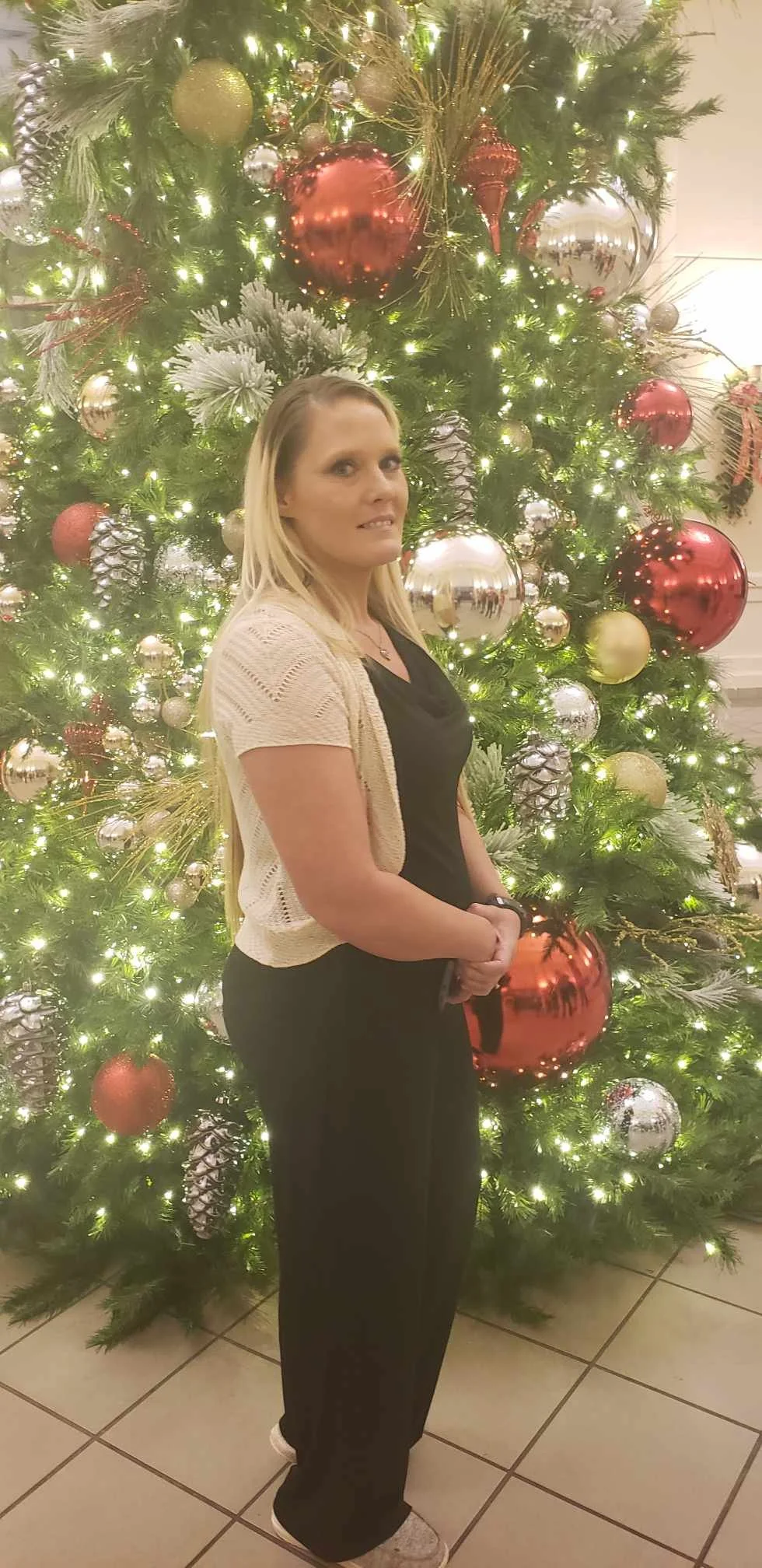 A woman standing in front of a decorated Christmas tree with ornaments and lights.