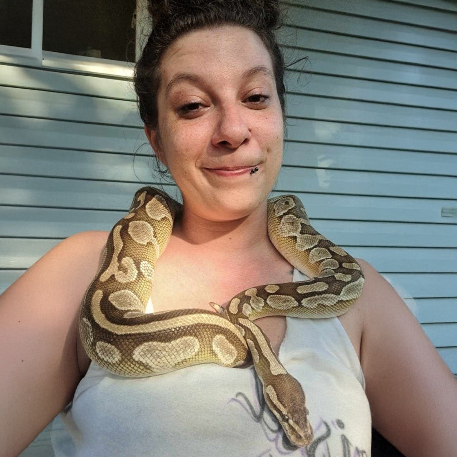 A woman with a snake draped around her shoulders, smiling.