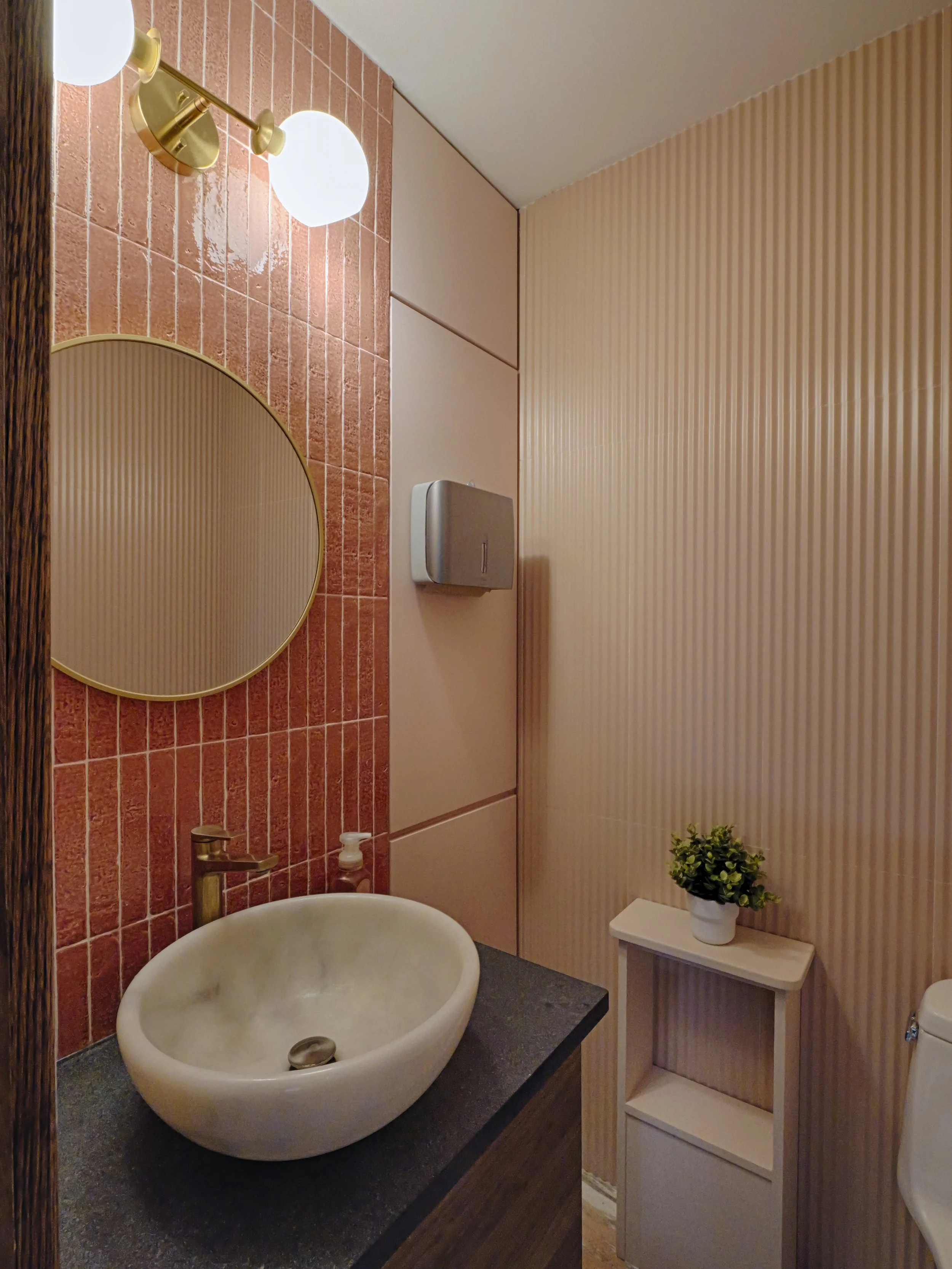 Commercial restroom renovation featuring textured pink tiles and modern vessel sink. High-quality interior design details for a Manhattan wellness space.