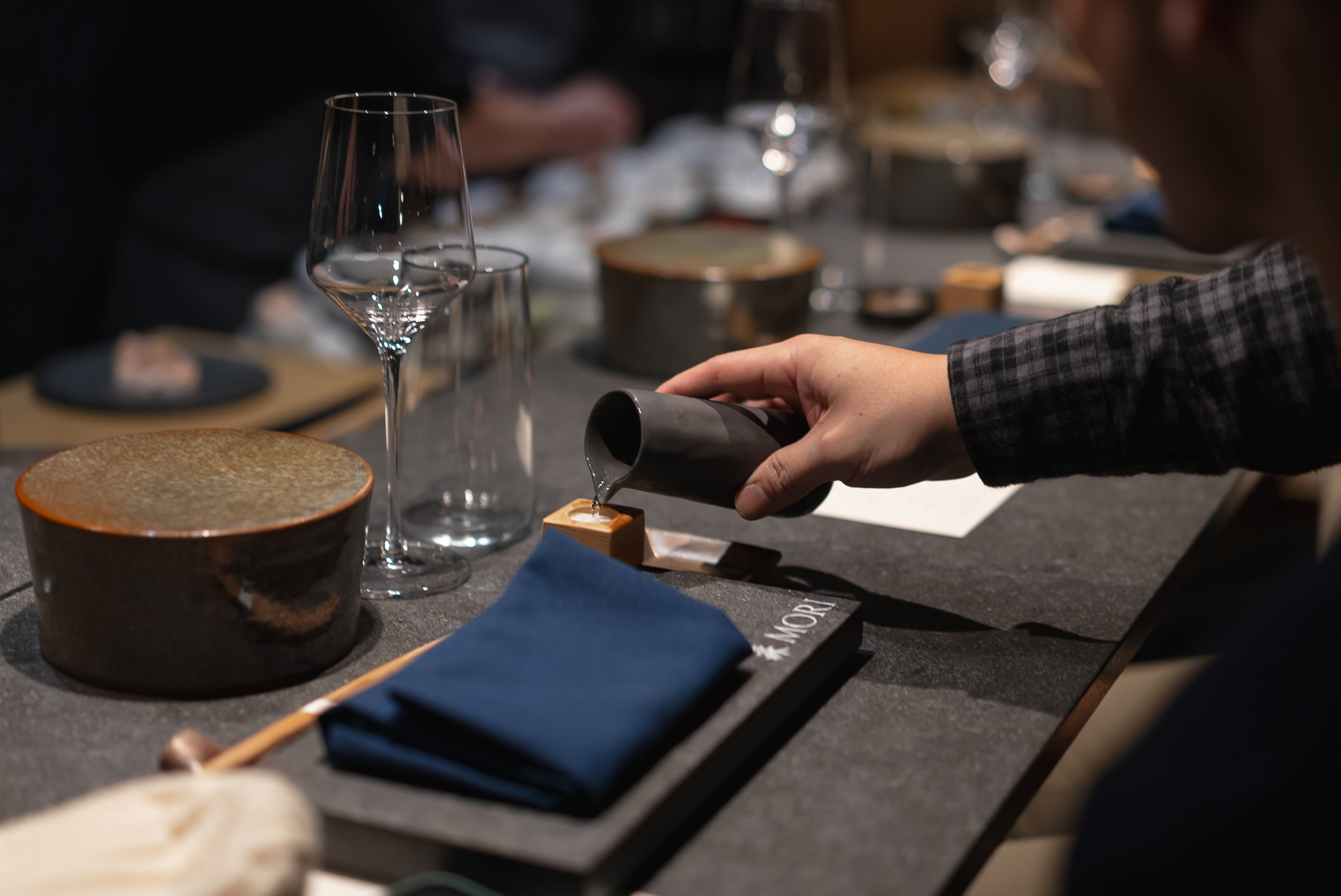 Atmospheric table setting at Mori Restaurant NYC. Showcasing the interaction between lighting design and tabletop surfaces in a high-end dining environment. Hospitality interior design by XZ Design Build.