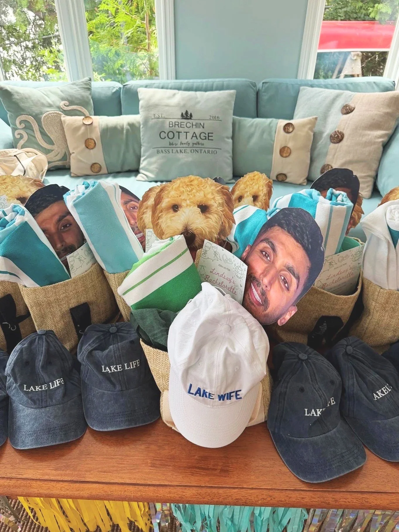 Collection of various hats and cutouts of people and a dog on a table, with a light blue sofa and cushions in the background.
