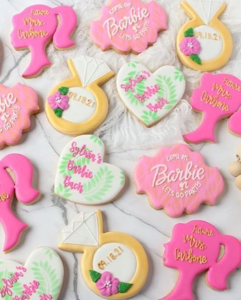 Decorated sugar cookies with pink, yellow, and white icing, featuring messages like "Come on Barbie, Let's Go Party" and "Sylvia's Bachelorette," along with purse, handbag, and floral designs for a celebration or themed event.