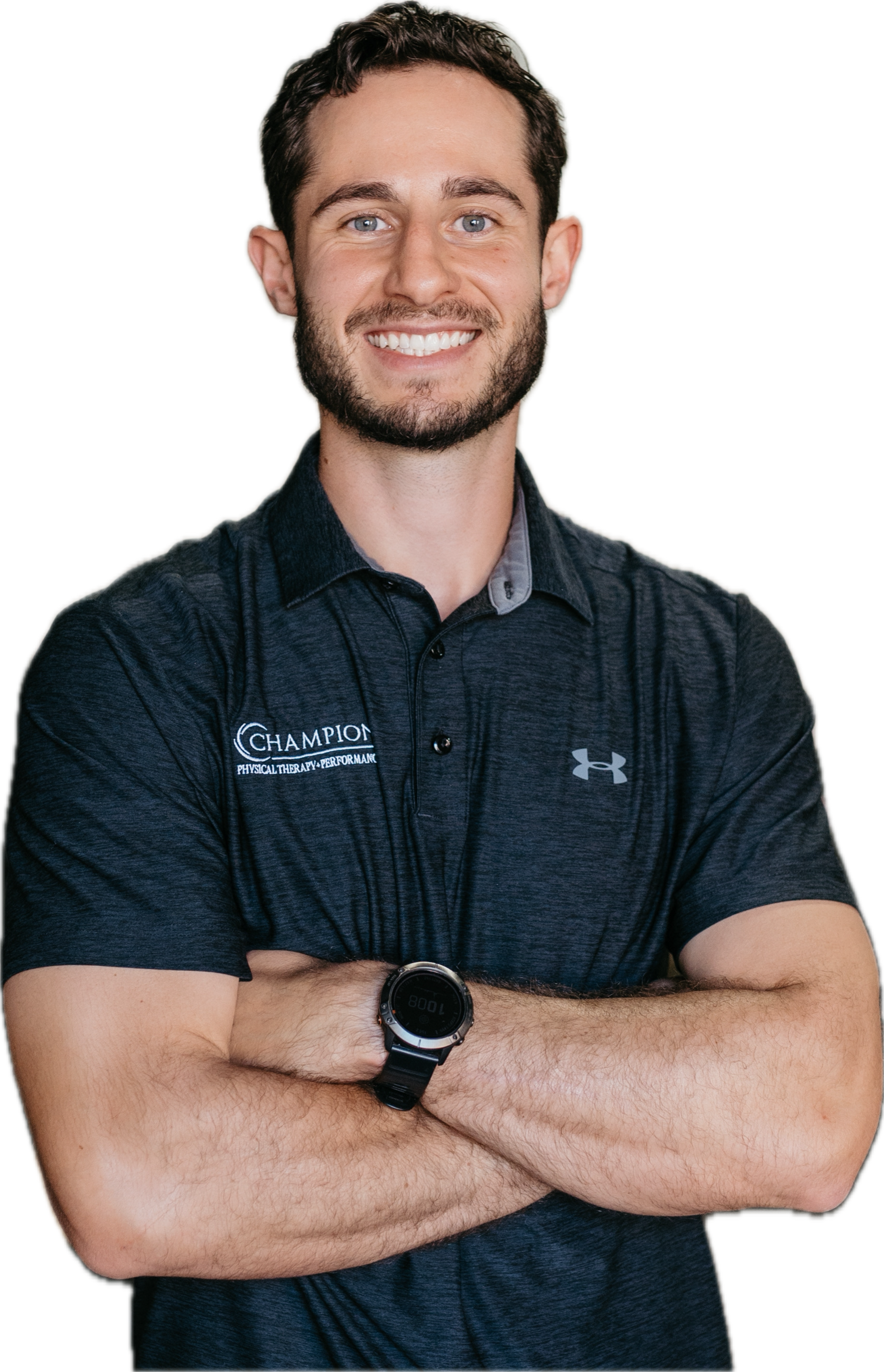 A smiling man with short dark hair, beard, and blue eyes, wearing a black Under Armour polo shirt with a logo that says 'Champion Physical Therapy Performance'. He is crossing his arms and wearing a watch on his left wrist.
