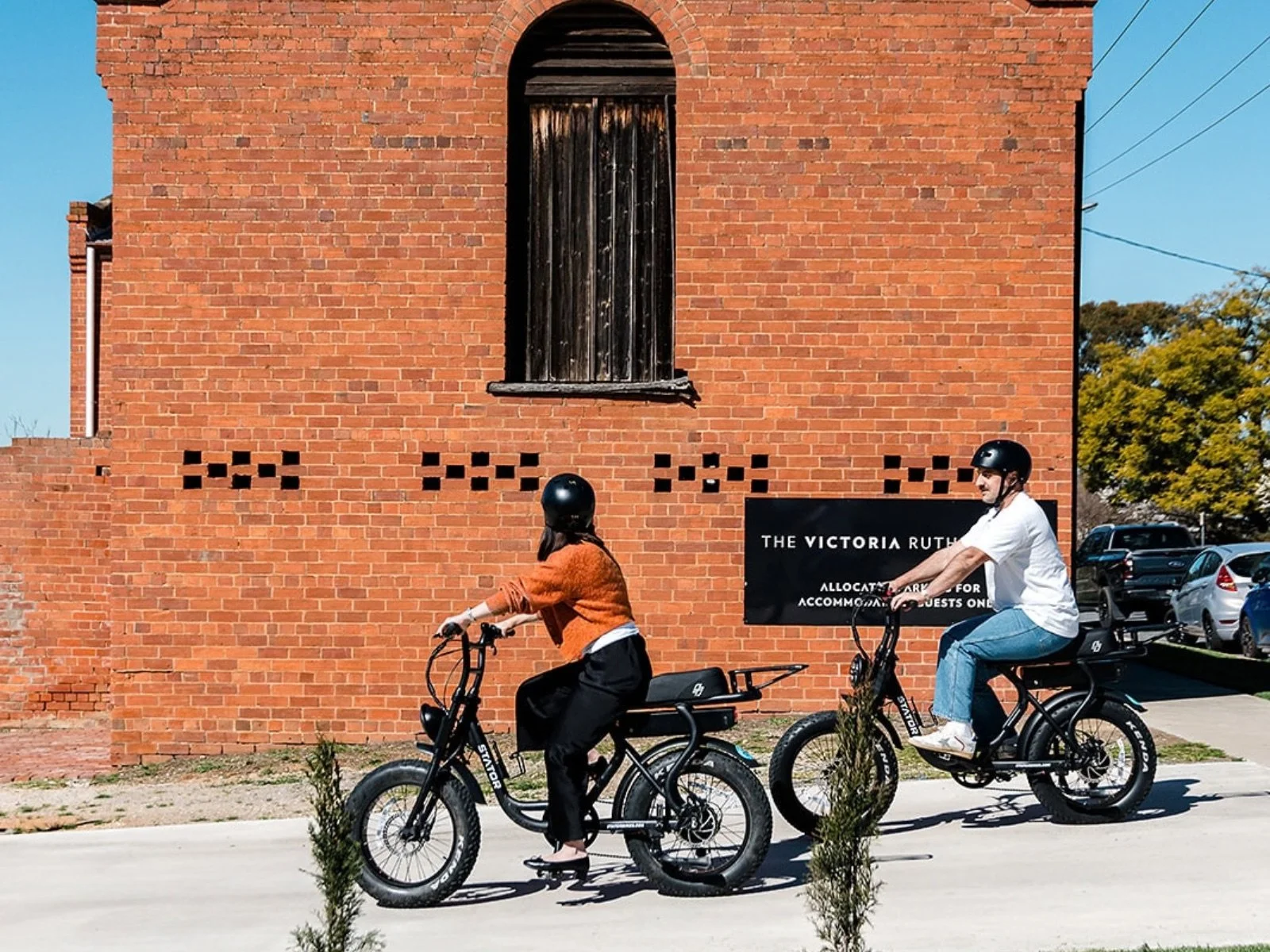 Guests riding e-bikes past the historic red-brick exterior of The Victoria Rutherglen