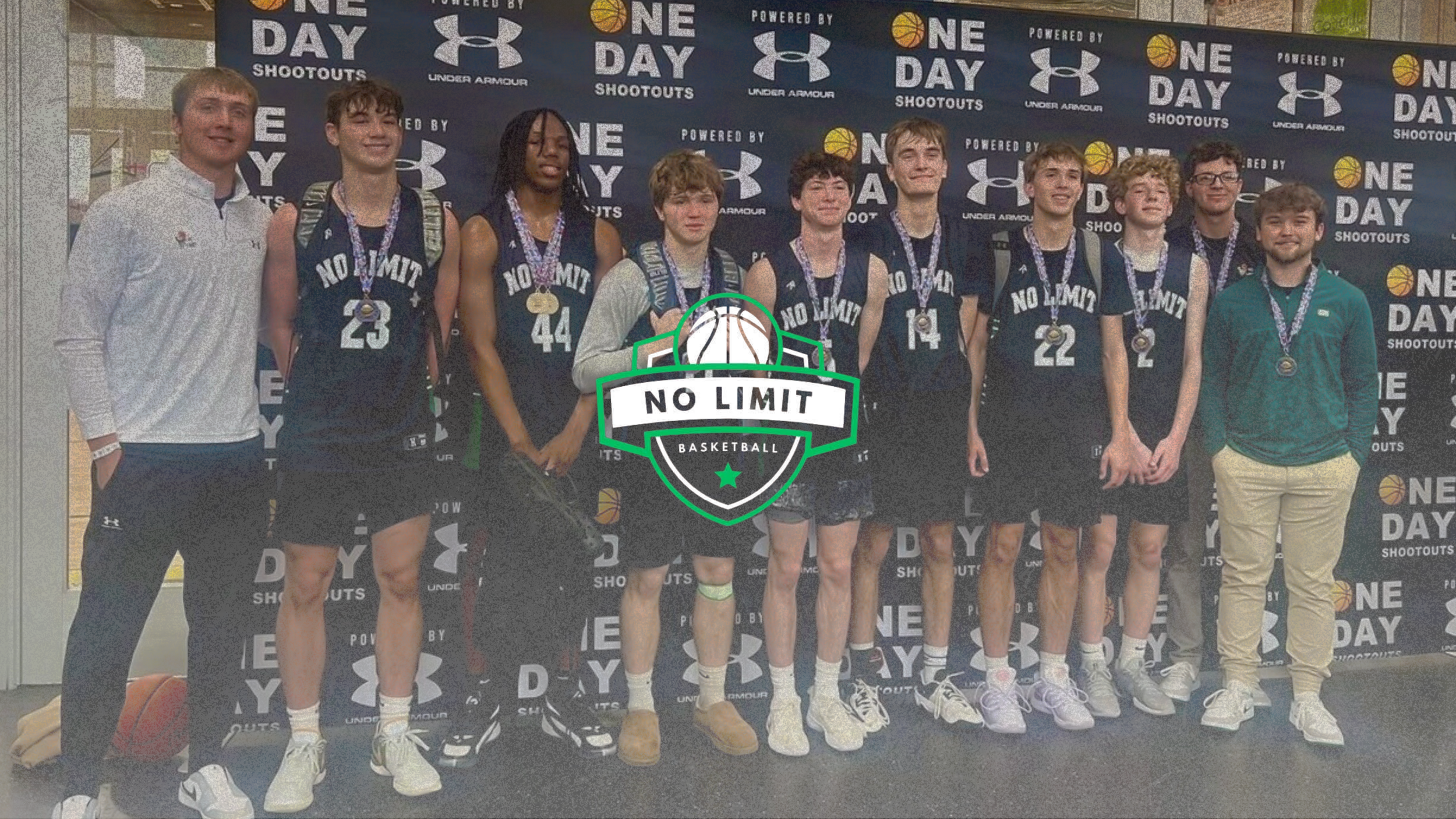 A group of young basketball players and a coach or staff member standing in front of a backdrop with logos for One Day Shootouts and Under Armour. The players are wearing basketball uniforms with medals around their necks, and they are holding hands or standing close together, celebrating their achievement.