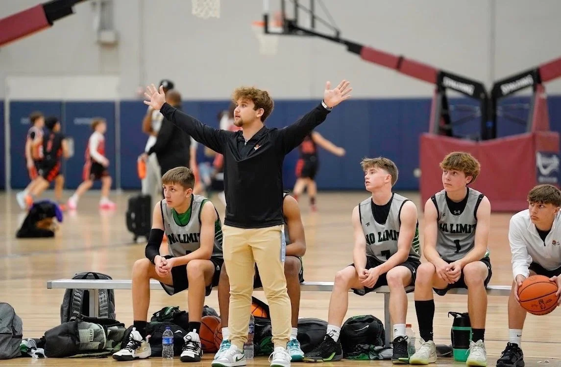 Basketball coach giving instructions to young players sitting on the bench during a game or practice.