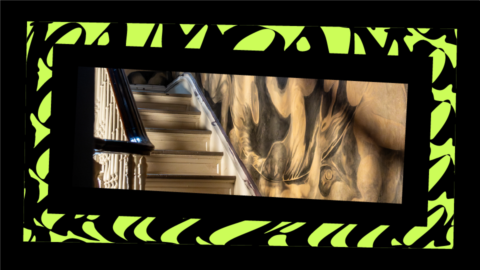 Close-up of a framed abstract painting with swirling beige, brown, black, gray, and cream colors, seen from a tilted perspective.