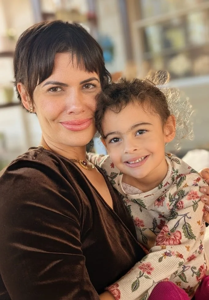 A woman with short dark hair and a young girl with curly hair smiling and hugging each other.