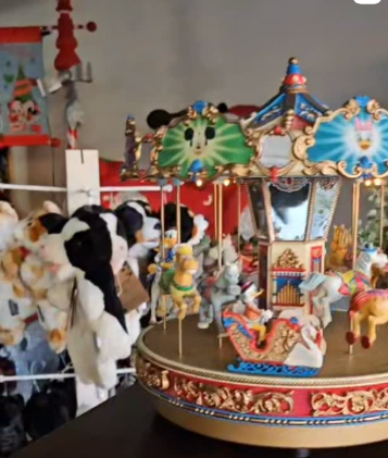 Colorful children's carousel toy with animals and characters, surrounded by stuffed animals in the background.