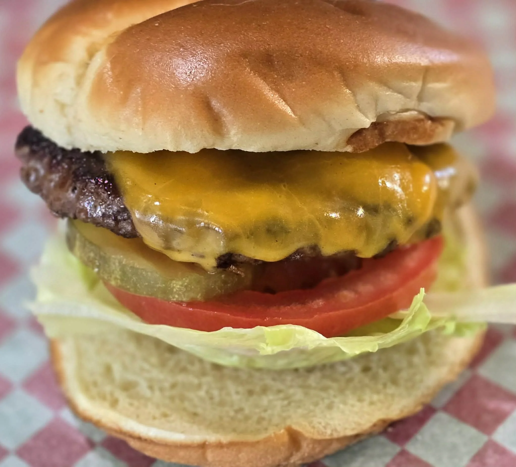 Close-up of cheeseburger with lettuce, tomato, pickles, beef patty, cheddar cheese, and a sandwich bun.