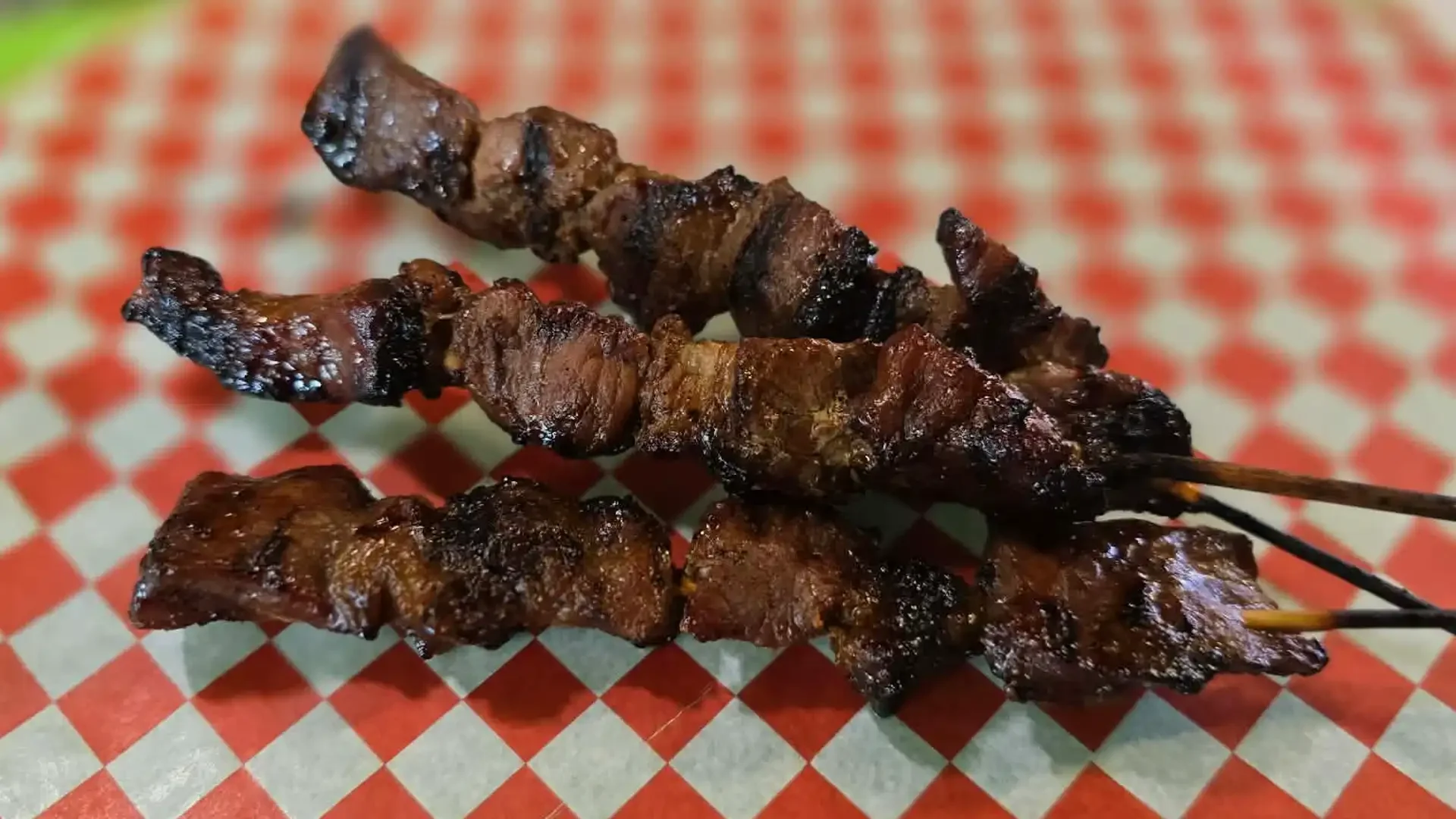 Two skewers of grilled meat on red and white checkered paper.