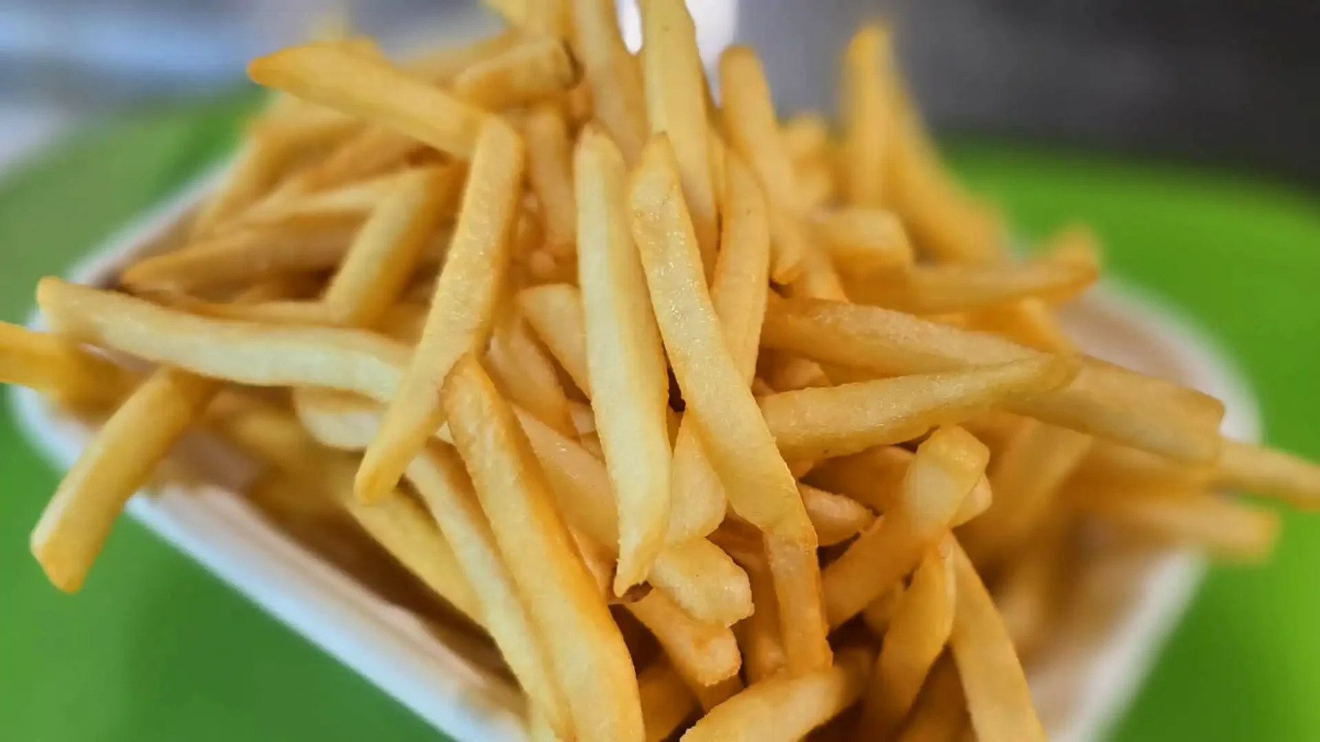French fries in a white container on a green surface.