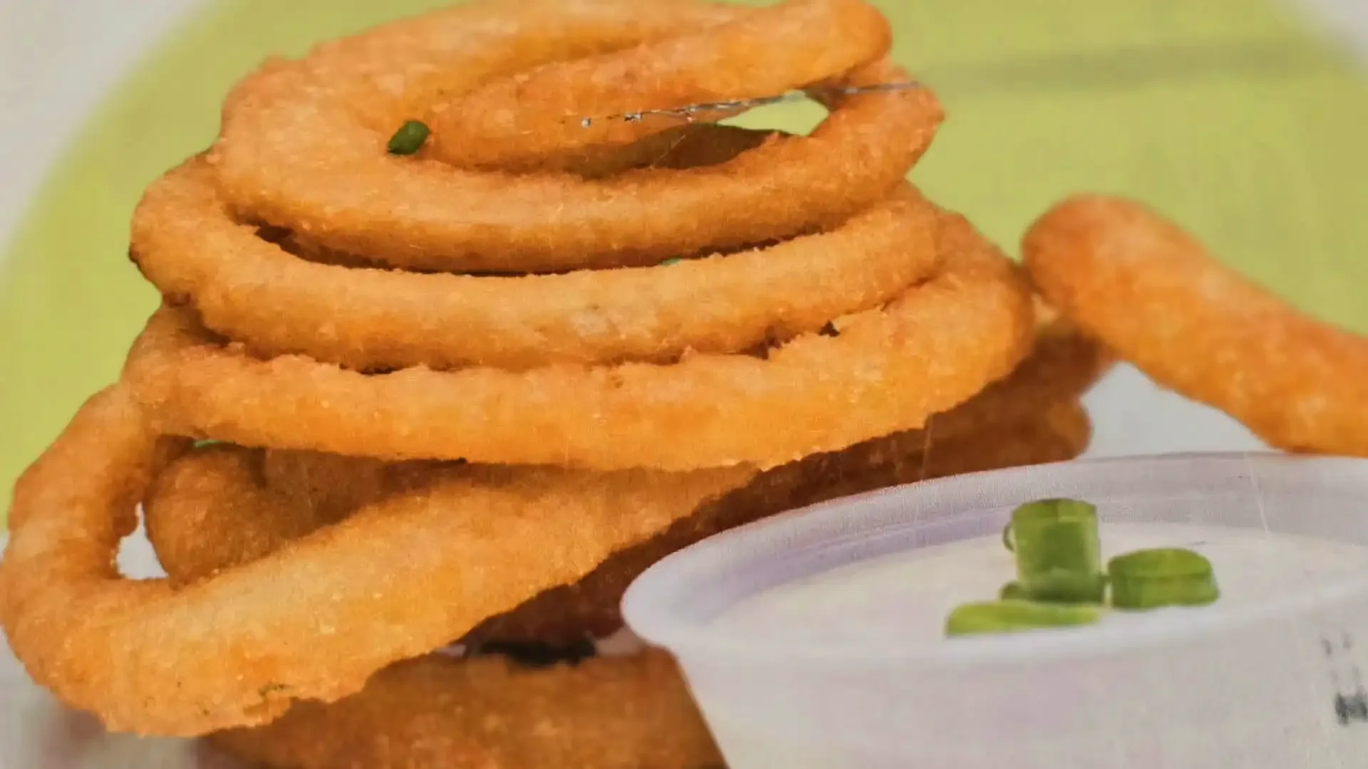 A stack of onion rings with a small container of dipping sauce garnished with chopped green onions.