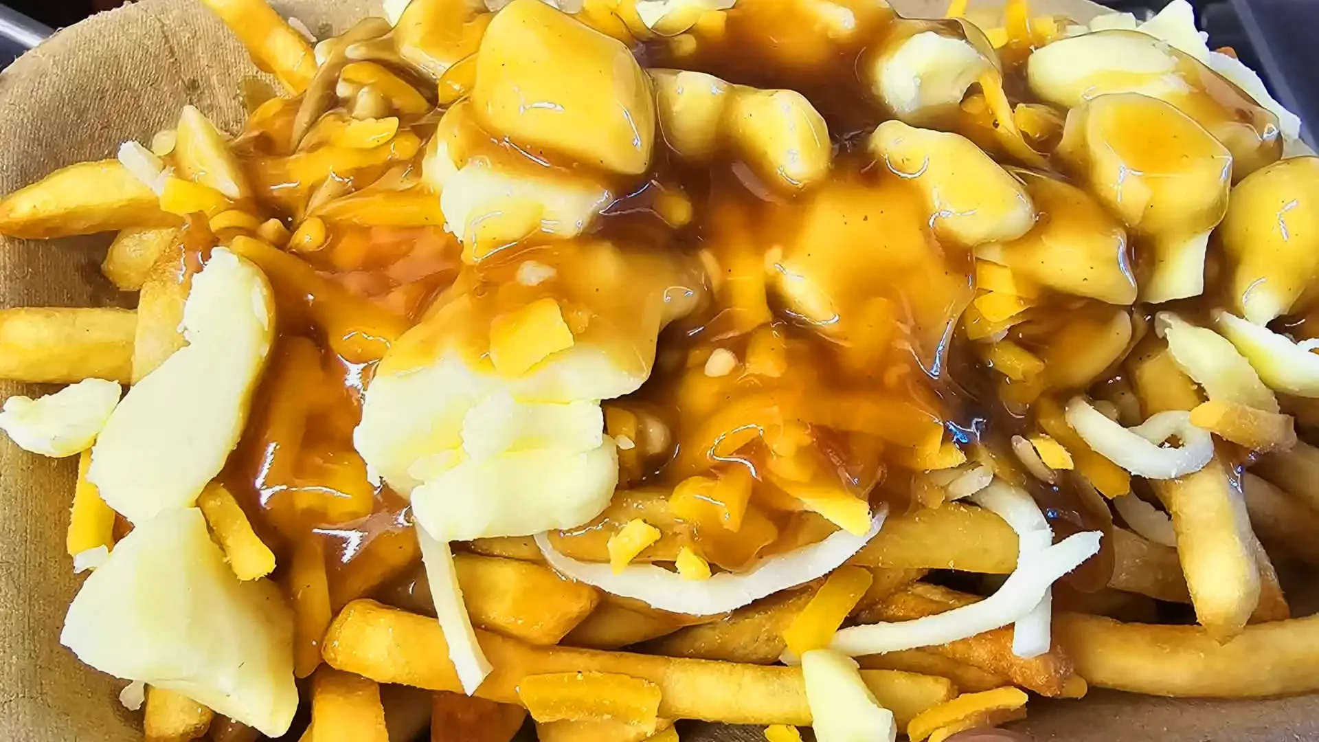 Serving of fries topped with shredded cheese, cheese slices, gravy, and pickles.