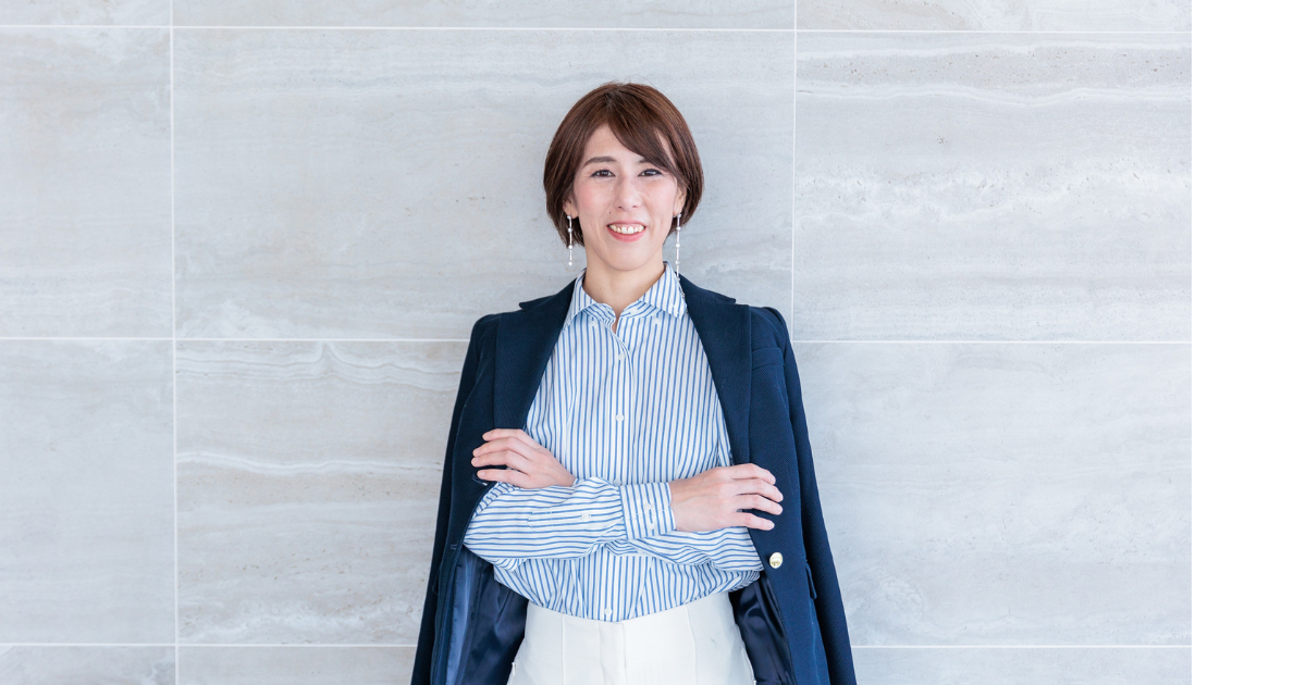 ビジネスカジュアルの服装をした女性が笑顔で立っている