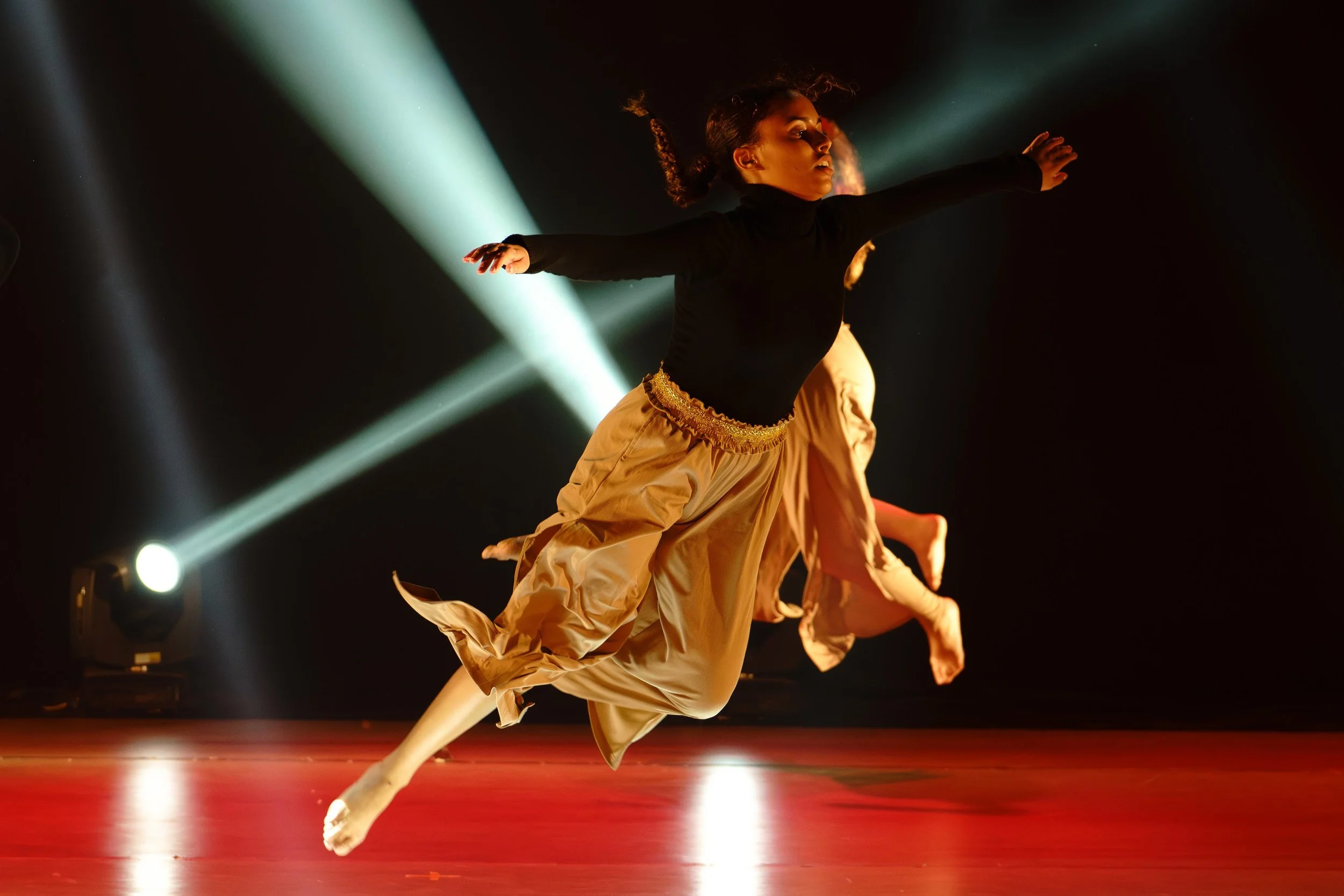 Two ballet dancers performing a leap on stage, with spotlights creating a dramatic background.