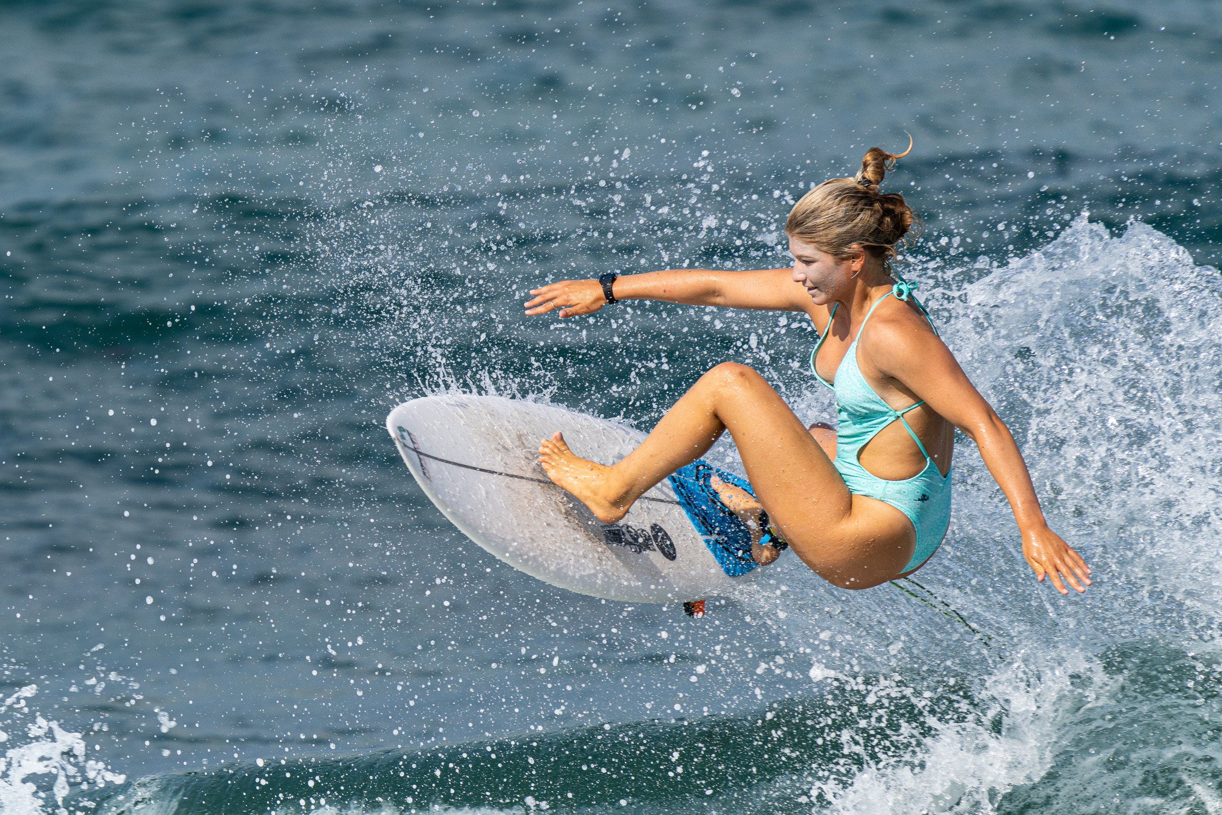 Young woman wearing a blue swimsuit riding a wave on a surfboard in the ocean.