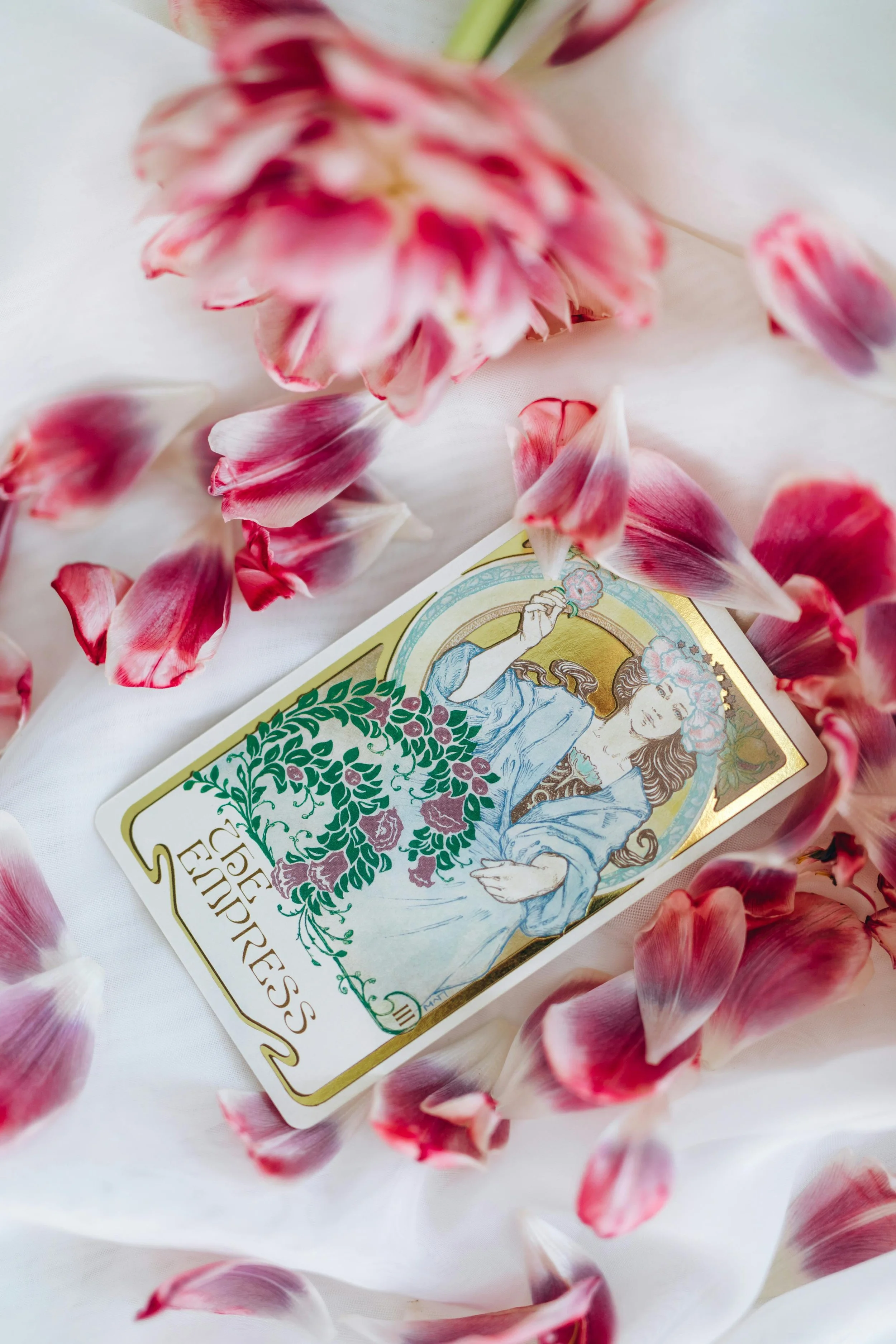 A tarot card titled 'The Empress' surrounded by pink and white rose petals on a white fabric surface.