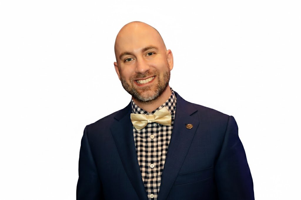 Headshot of Dirk in a blue blazer, checkered shirt and gold bowtie.