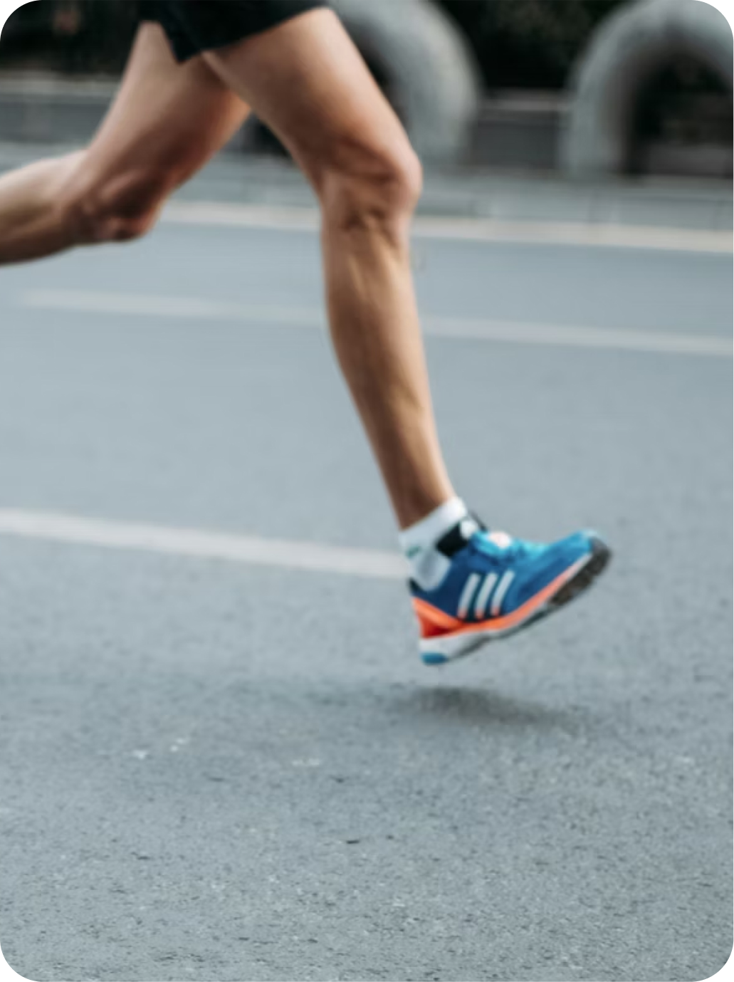 Close-up of a runner's legs in motion on an outdoor road, wearing athletic shoes and black shorts.