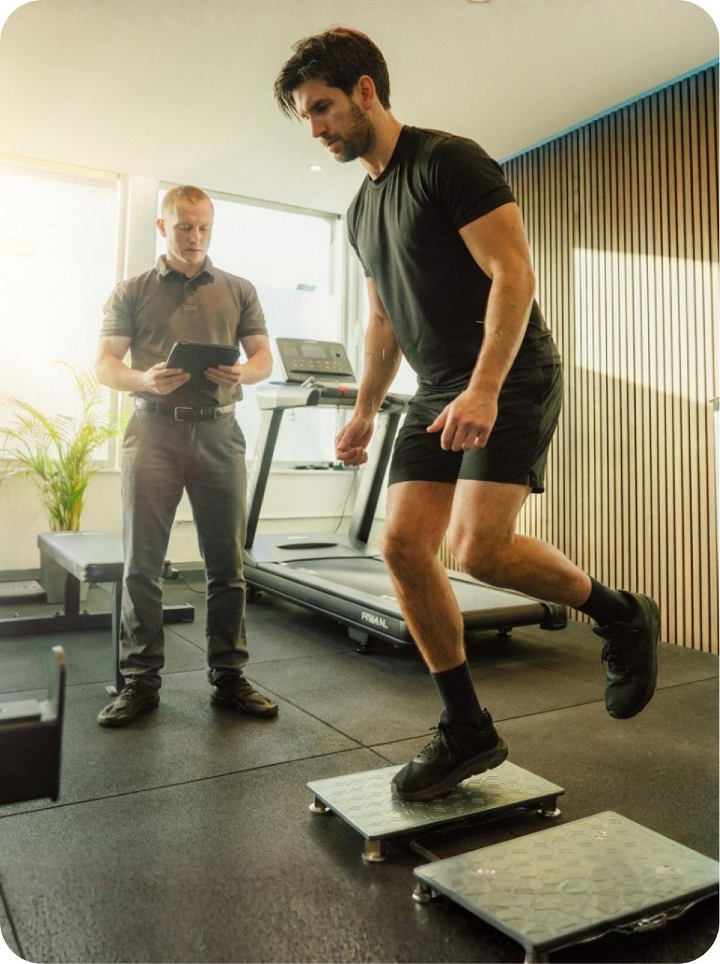 Man wearing black athletic clothes doing a force testing jump while the physiotherapist observes