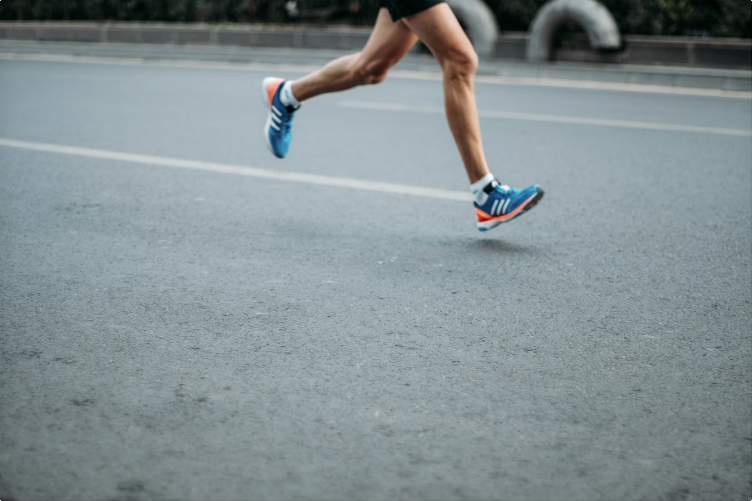 A person running on a paved road, wearing blue running shoes, black shorts, and a black shirt.