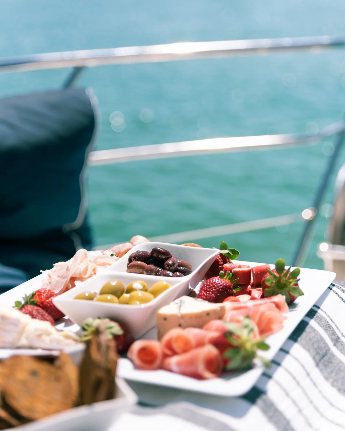 A platter of assorted cheeses, strawberries, olives, and berries on a boat with water in the background.