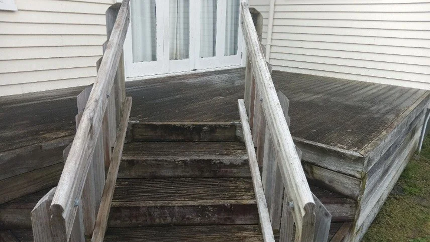Wooden steps leading up to a sliding glass door on a weathered deck.