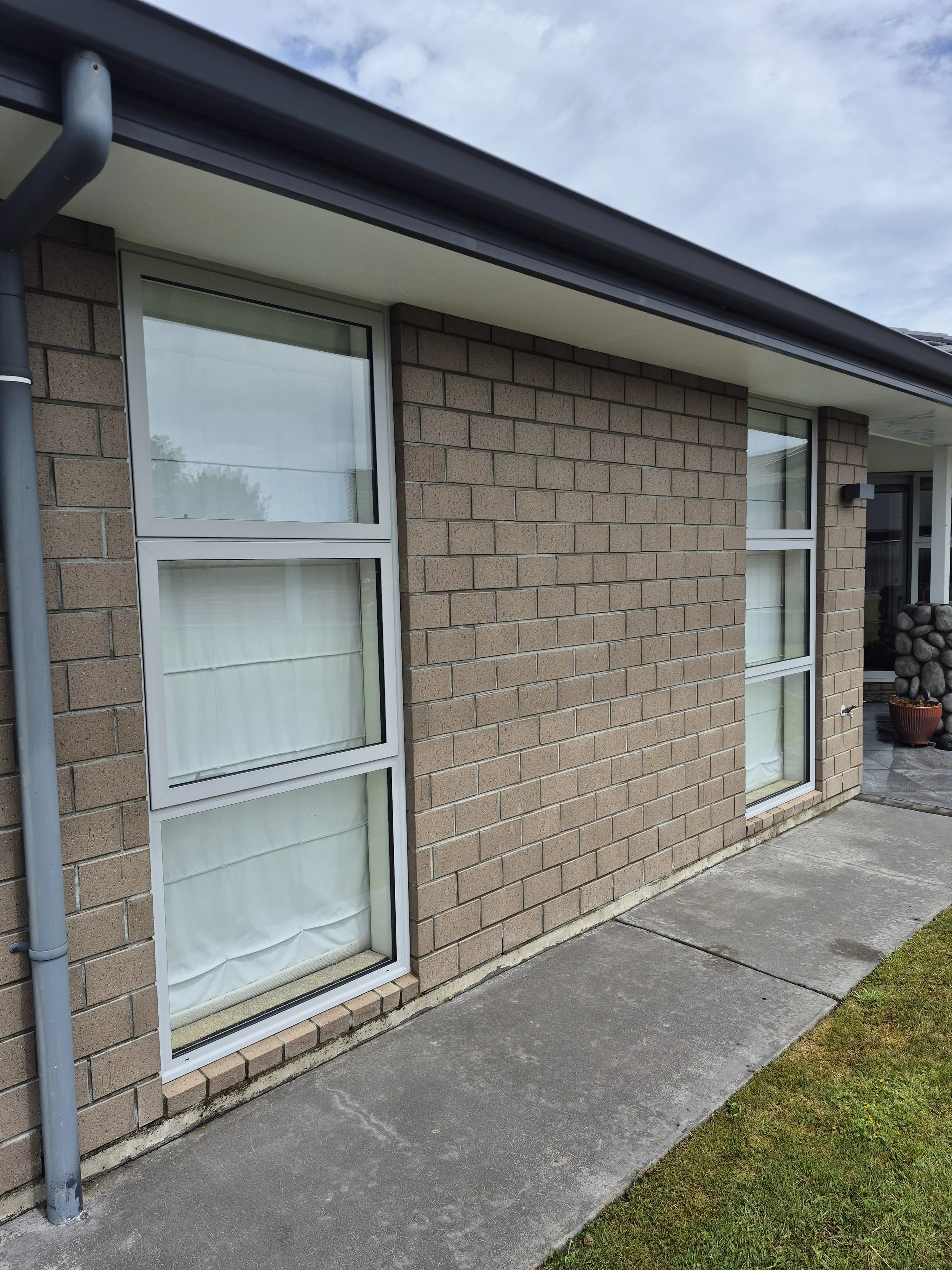 Exterior view of a brick house with two sliding windows, a concrete sidewalk, and a small patch of grass.