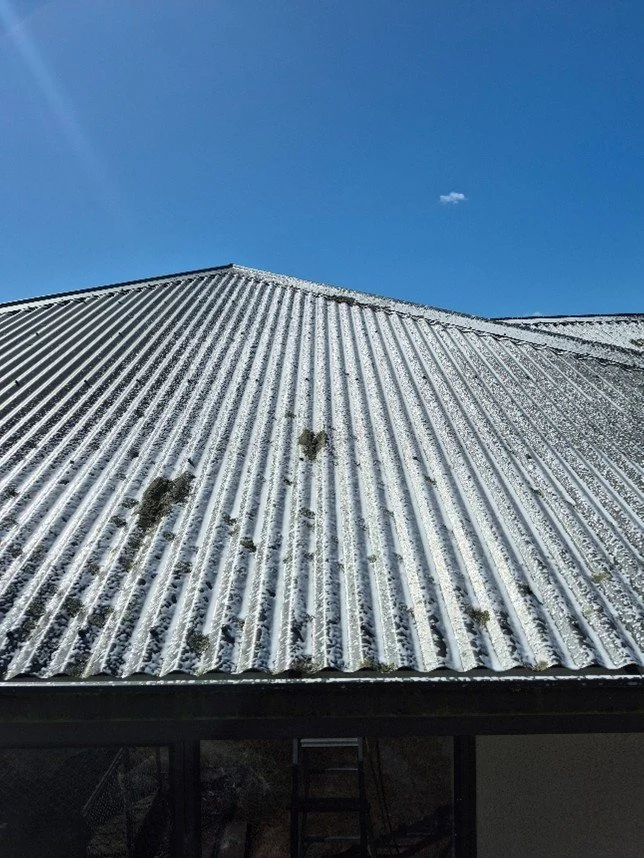 Metal rooftop with patches of snow and ice, under a clear blue sky with a small cloud.