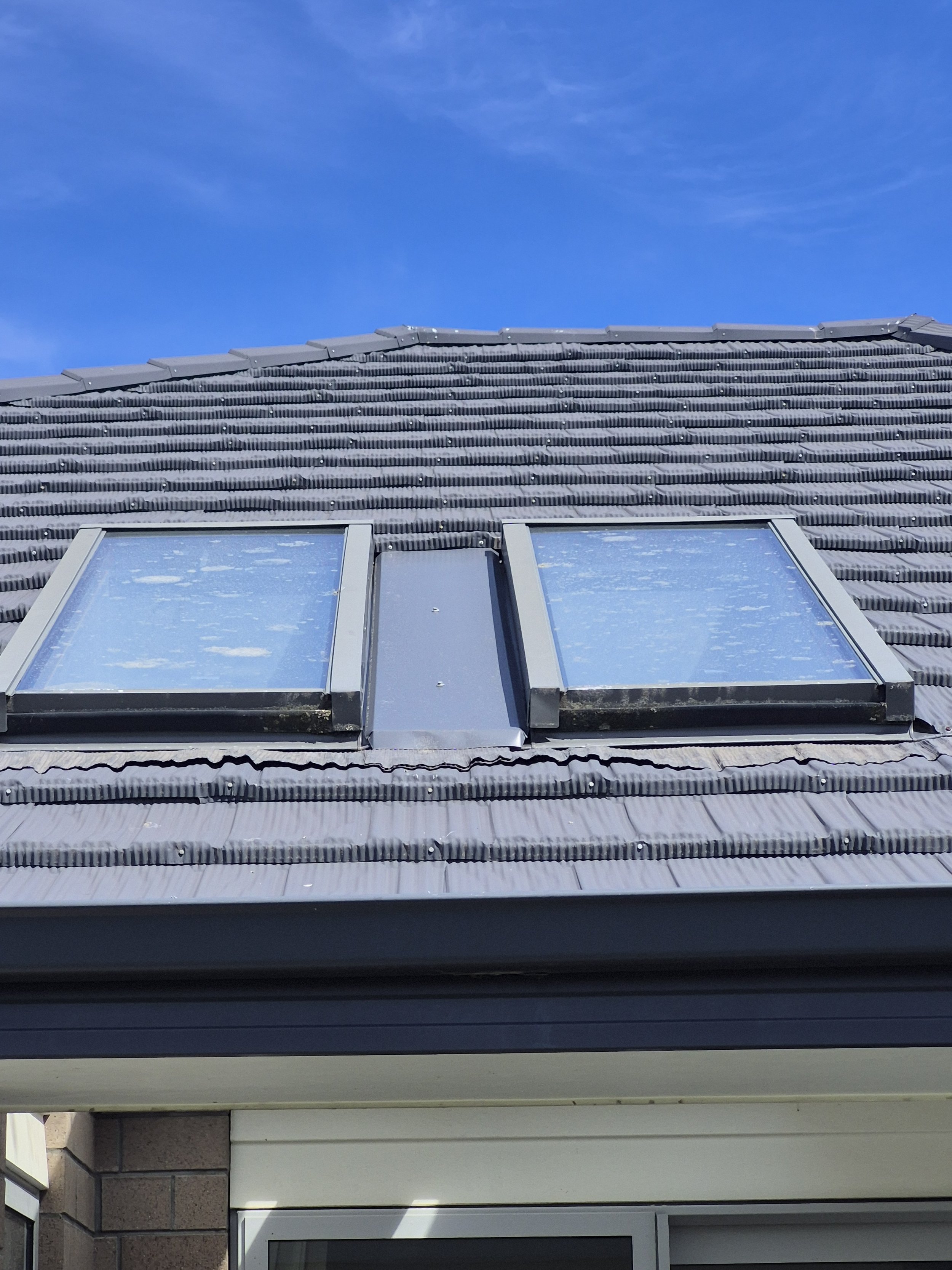 Upward view of a house roof with two skylights and a blue sky.