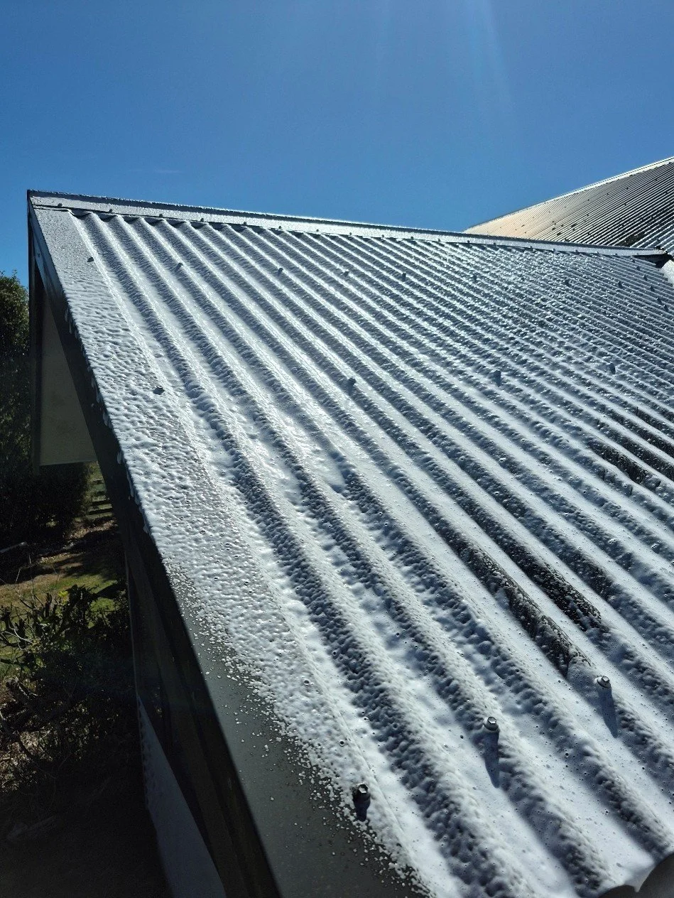 Close-up of a metal roof with residual snow and ice, under a clear blue sky.