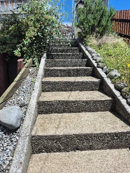 Concrete outdoor staircase with gravel and plants on each side, leading toward a gated backyard.