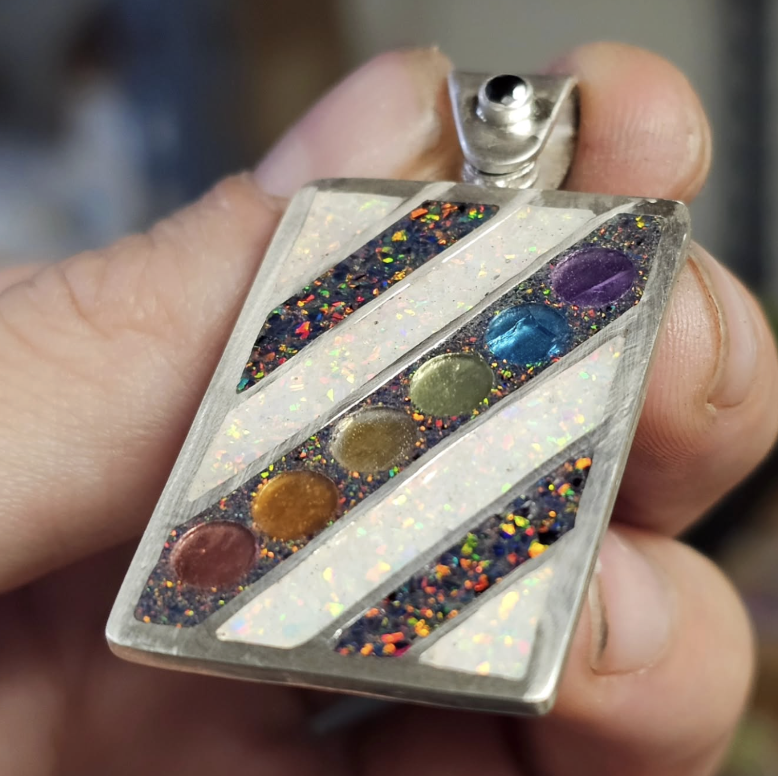 A person holding a metallic vape device decorated with colorful inlays and holographic details.