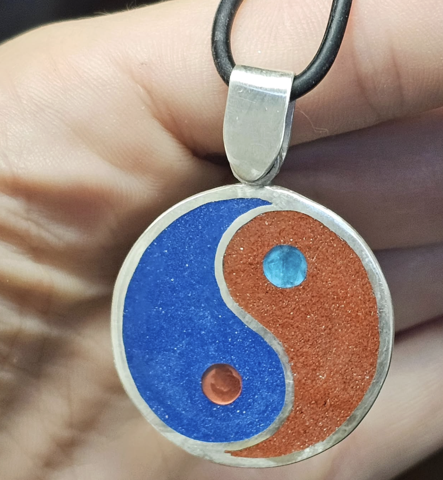Yin-Yang pendant with blue and orange colors, held by a person's fingers.