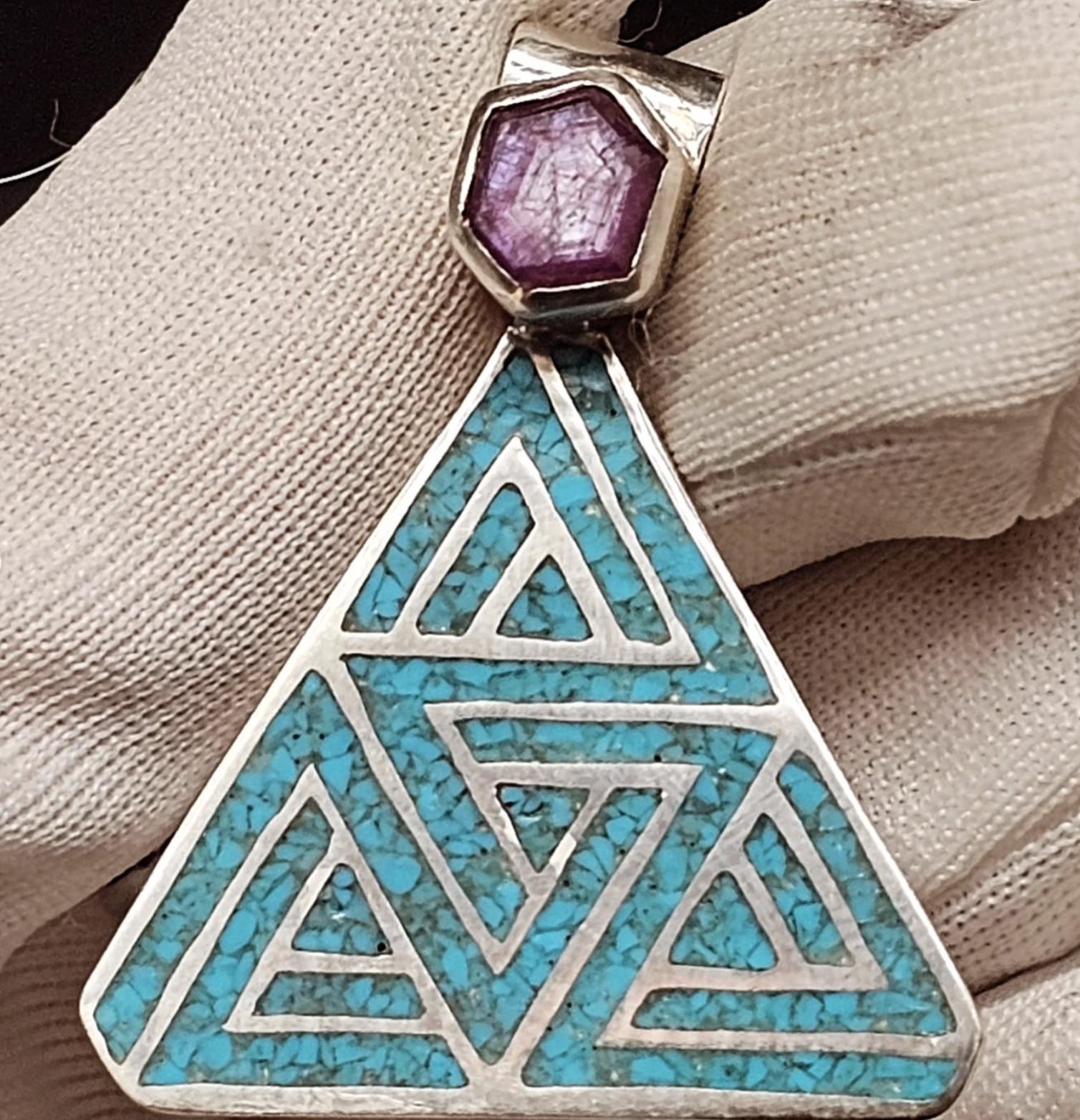 A silver pendant with a purple hexagonal stone connected to a large triangular turquoise inlay with geometric cutouts.