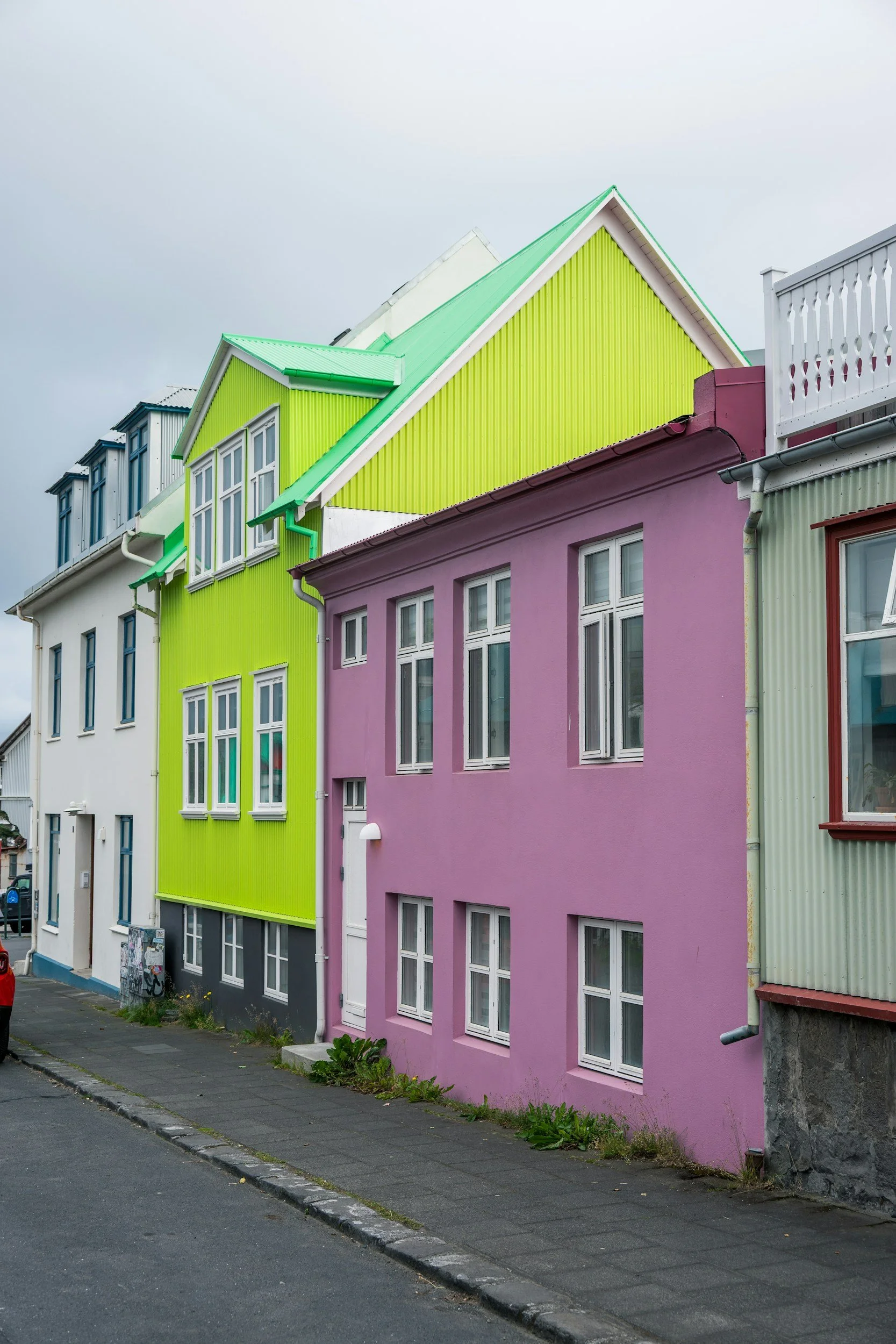 Edificio de casas coloridas en una calle, con fachadas rosa, verde y blanca, ventanas blancas y cielo nublado.