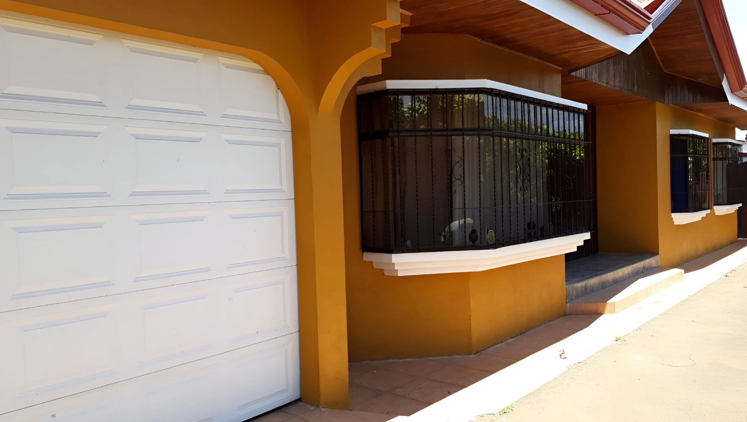 Casa con muro amarillo, ventanas con rejas negras y cochera con puerta blanca.