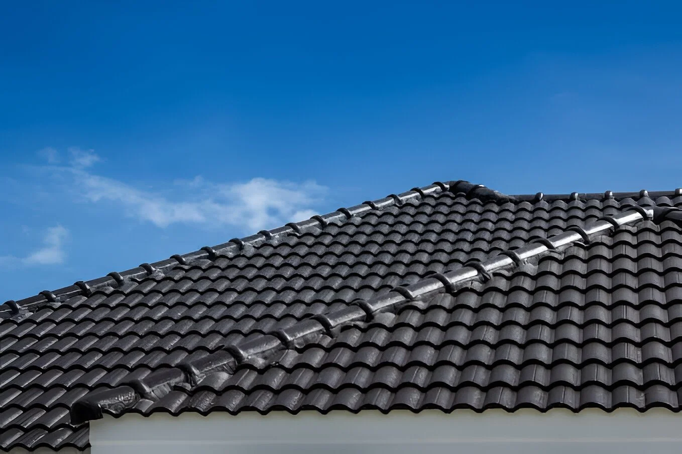 Techo de tejas negras bajo un cielo azul con algunas nubes