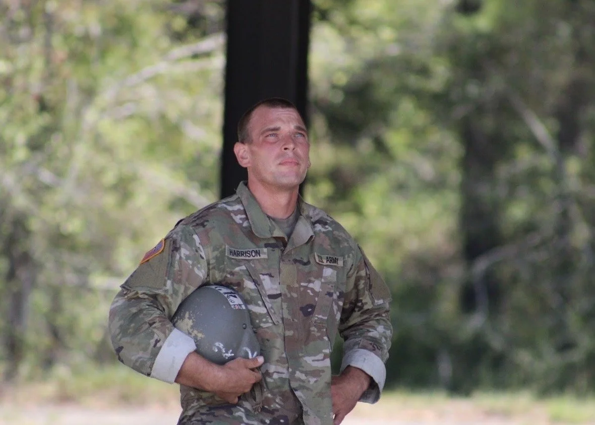 Airborne soldier holding his helmet while watching fellow soldiers during training