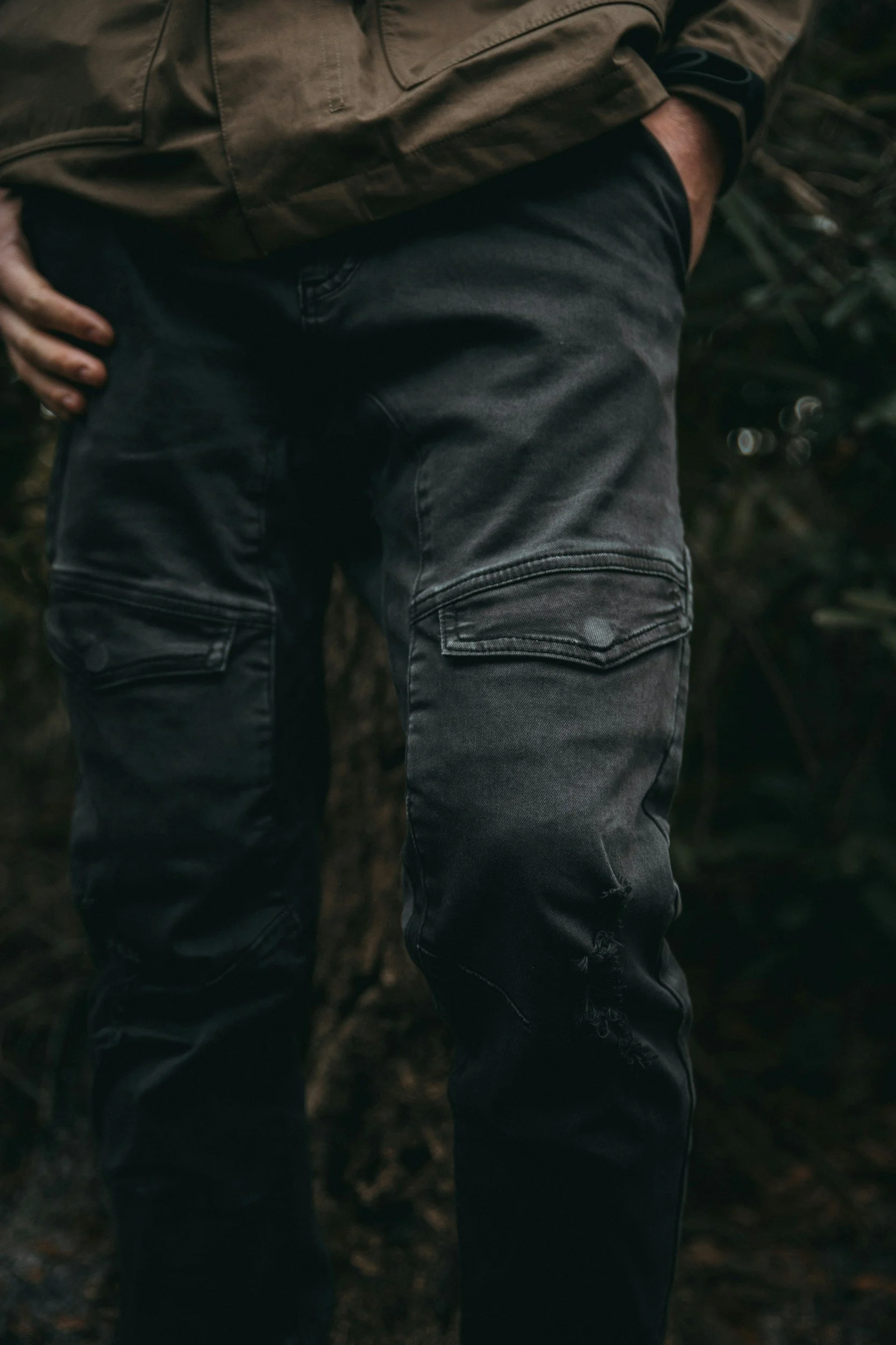 Close-up of a person wearing black jeans and a beige jacket, standing outdoors.