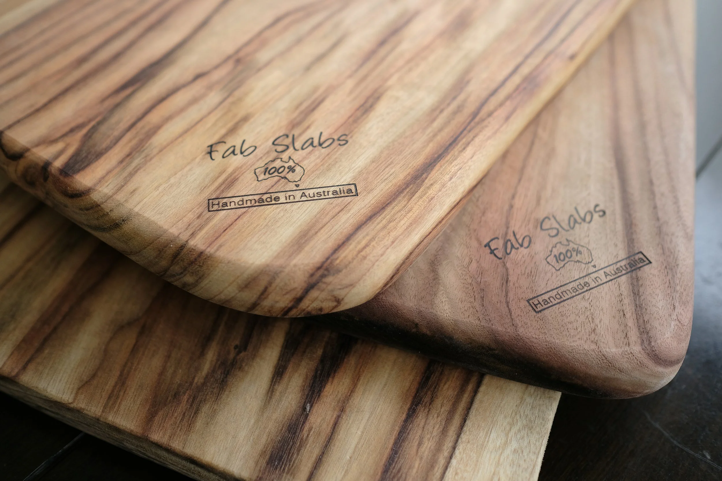 Close-up of a wooden cutting board with the words "Fab Slabs" and "100%" inside an outline of Australia, along with the phrase "Handmade in Australia" printed on it.