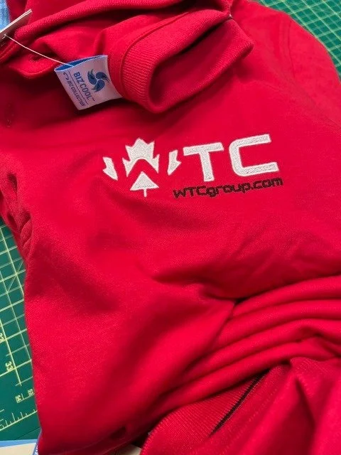 Close-up of red clothing with WITC logo and website, lying on a green cutting mat.