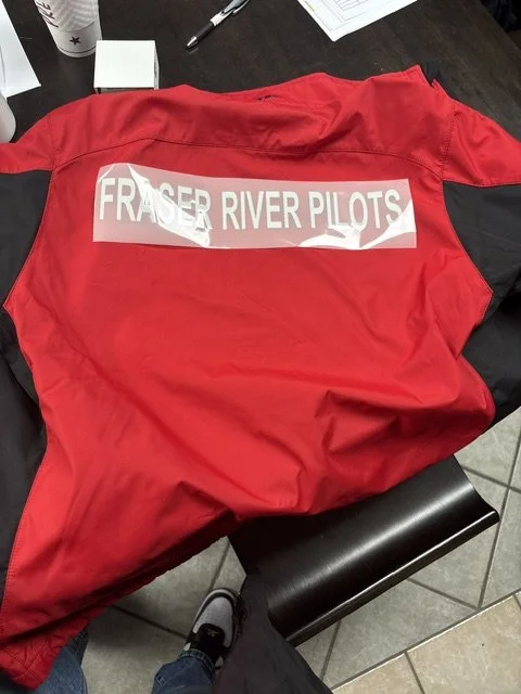Red jacket with a patch that says "FRAZER RIVER PILOTS" on the back, resting on a black chair at a desk.