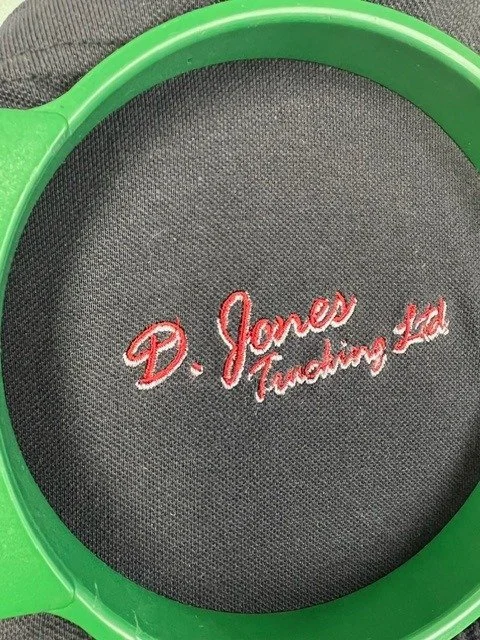 A black tennis racket head with red embroidered text that reads 'D. Jones Tennis Led', partially surrounded by a green tennis racket frame.