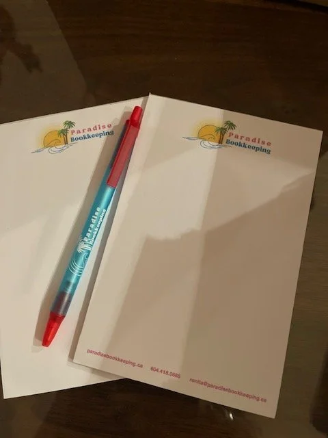 Two sheets of paper with a logo of a sunset and palm trees, a red and teal pen, and a wooden surface.
