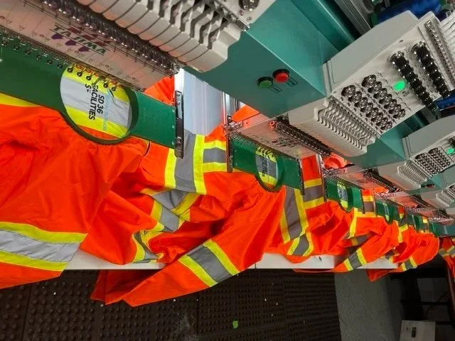 Bright orange safety vests with reflective stripes hanging on electrical control panels.