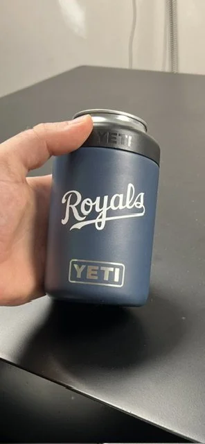 A hand holding a blue Yeti Royals beverage container on a gray surface.