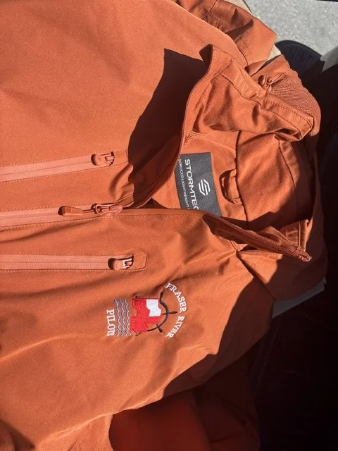 Orange outdoor jacket with a Stormtech logo and a patch that says 'First Ascent' with a mountain and lake design.